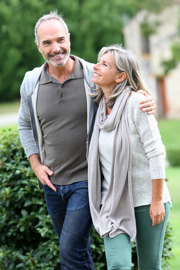 A mature couple in gray toned clothes and jeans walk happily outside, happy with their successful bioidentical hormone treatments from Tanya Zboril, NP of TBT Medical in Regina.