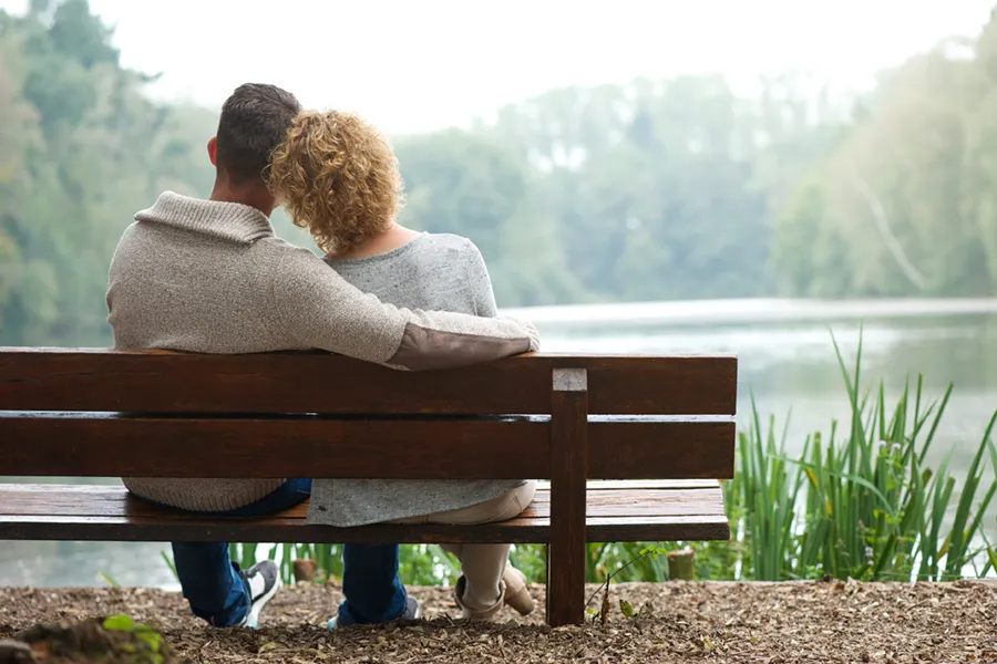A couple wearing sweaters seen from behind sitting on a bench and looking out at a relaxing lake and forest, representing functional medicine treatment from Tanya Zboril, NP of TBT Medical in Regina.