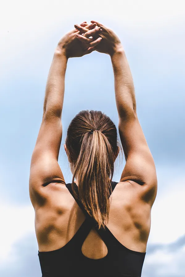 A toned woman seen from behind stretching her arms into the air. Get GLP-1 Weight Loss Injections from Tanya Zboril, NP of TBT Medical in Regina.