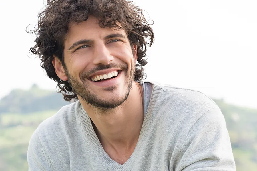 A man with radiant curly hair and a confident smile looks to the horizon. Tanya Zboril, NP of TBT Medical in Regina offers effective therapies to support hair regrowth and scalp health to treat hair loss.