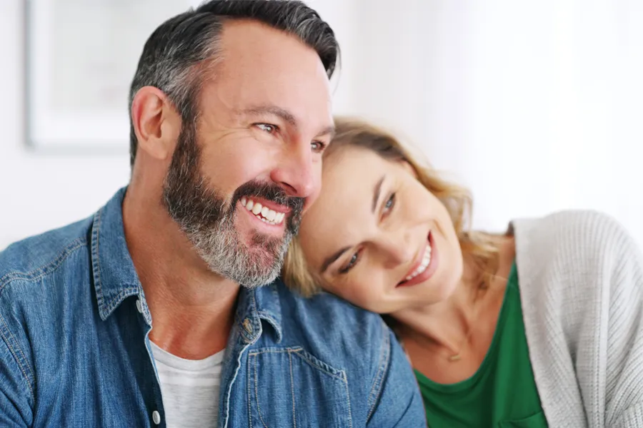 A middle-aged white couple in a bright white room smile and lay their heads on each other. Schedule concierge health and wellness services from Tanya Zboril, NP of TBT Medical in Regina.