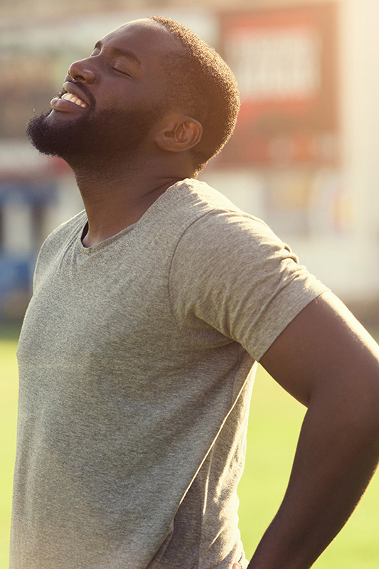 Lean-Muscle-and-Recovery-Treatment A black man in a gray t-shirt and smiles, looking up with closed eyes after a satisfying workout. Get treatment for lean muscle loss and recovery from Tanya Zboril, NP of TBT Medical in Regina.