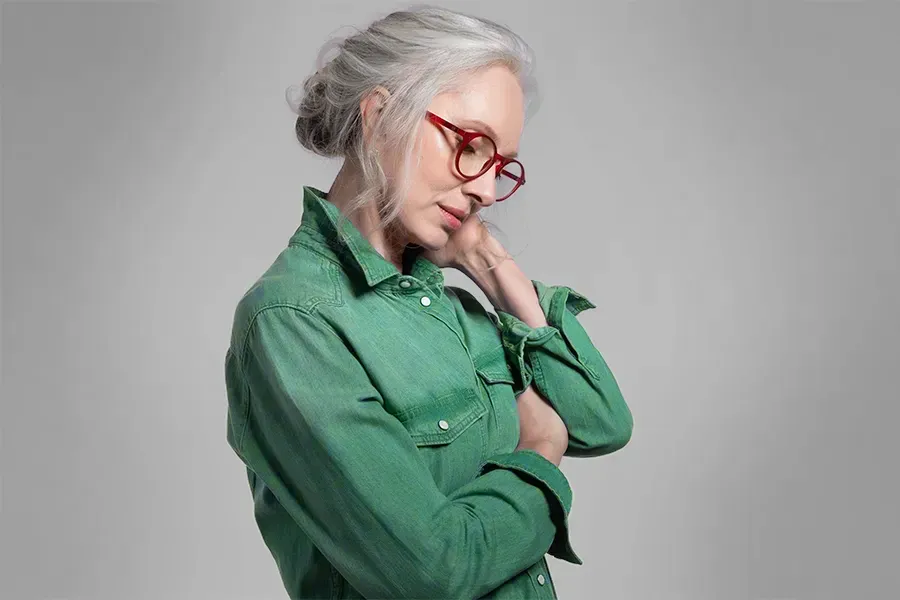 A middle-aged woman in a green shirt holds her neck and grimaces in pain. Schedule low dose naltrexone treatment from Tanya Zboril, NP of TBT Medical in Regina.