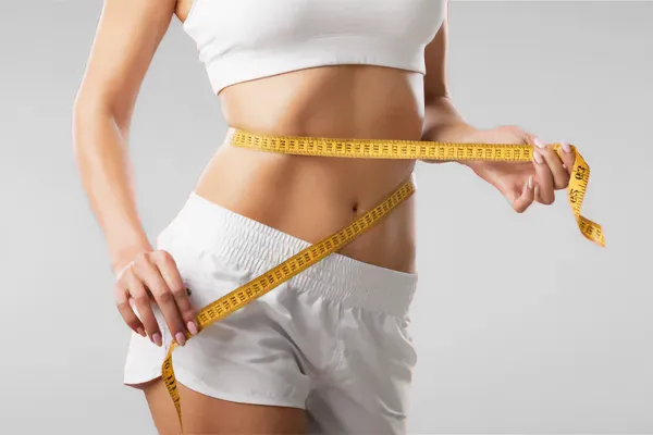 A woman wraps a measuring tape around her waist to show the success of her Low Dose Naltrexone for Weight Loss treatments from Tanya Zboril, NP of TBT Medical in Regina.