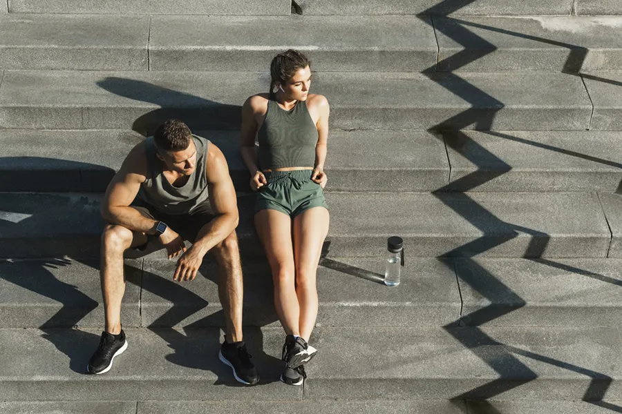 A couple in gray and green track clothes resting after a workout on stone steps, happy with their weight loss plans from Tanya Zboril, NP of TBT Medical in Regina.