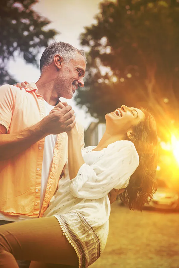 A middle-aged couple dances playfully in the woods at sunset. Get Metformin for weight loss treatment from Tanya Zboril, NP of TBT Medical in Regina