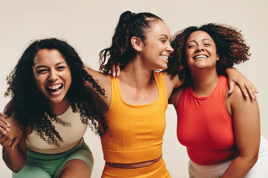Three healthy women in colorful clothes laugh arm in arm. Schedule Mounjaro for weight loss from Tanya Zboril, NP of TBT Medical in Regina.