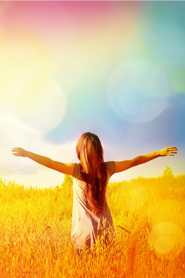 Woman standing in a golden field with arms outstretched toward a vibrant, rainbow-hued sky, symbolizing vitality and inner renewal with NAD Therapy offered by Tanya Zboril, NP of TBT Medical in Regina.