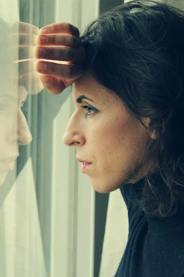 A brunette woman in a thin dark turtleneck looks out the window with a serious expression, suffering from PCOS. Get treatment for Polycistic Ovarian Syndrome/PCOS from Tanya Zboril, NP of TBT Medical in Regina.