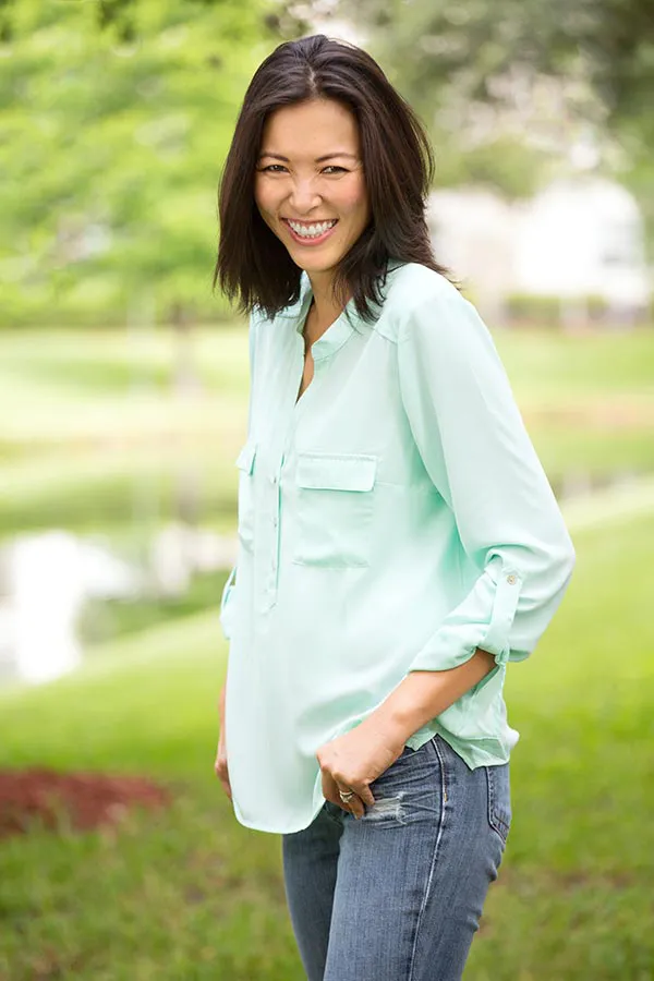 A middle-aged brunette woman in a light green button-up shirt stands outside smiling, happy with her perimenopause treatment from Tanya Zboril, NP of TBT Medical in Regina.