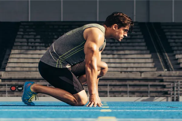 With a determined look, Aamuscular man in track clothes kneels at the start of a race. Get Sermorelin peptide therapy from Tanya Zboril, NP of TBT Medical in Regina.