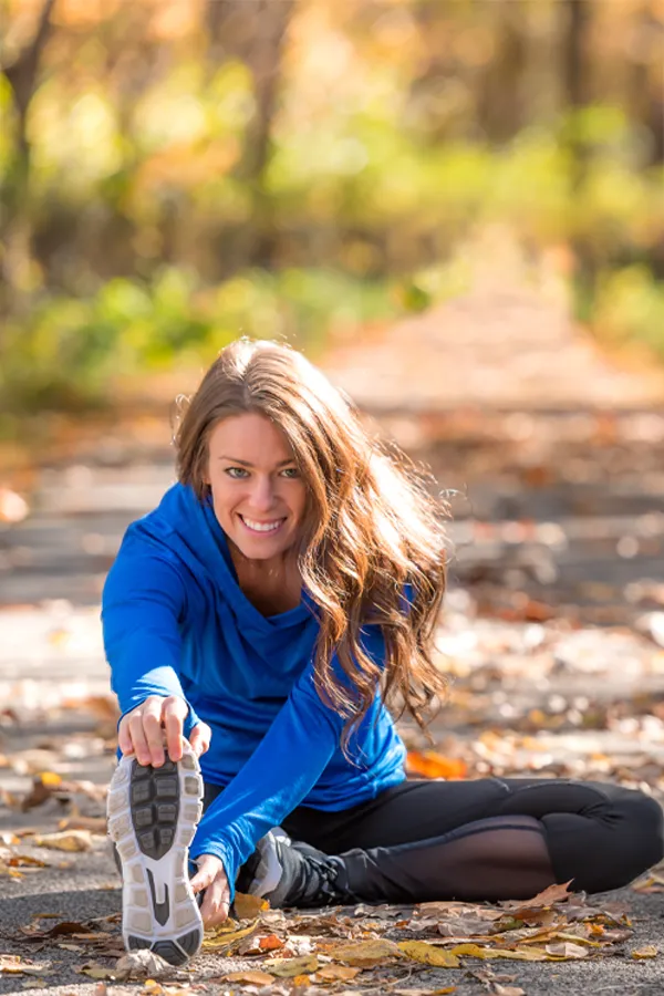 A healthy woman in blue sweats stretches on a trail before a run. Get Sermorelin peptide therapy from Tanya Zboril, NP of TBT Medical in Regina.