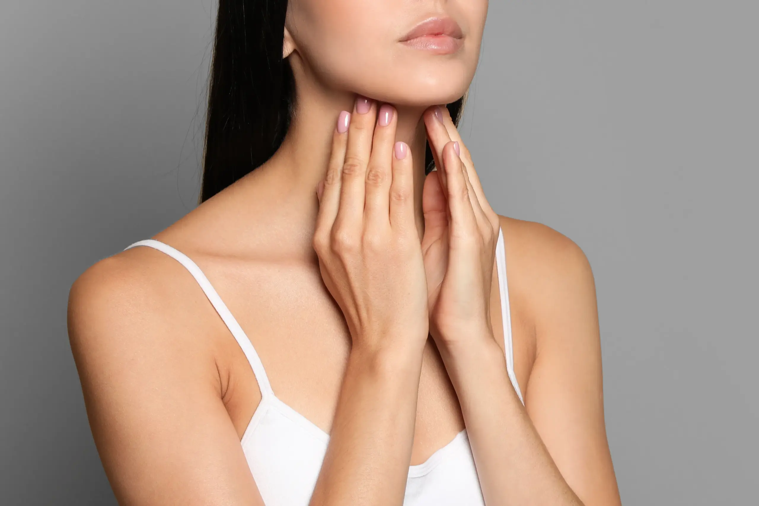 A woman in a white tank top touches her neck looking for signs of thyroid disorder. Get help for thyroid disorders from Tanya Zboril, NP of TBT Medical in Regina.
