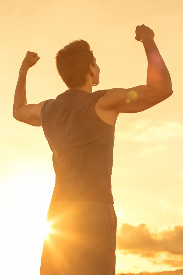 A motivational image of a young man standing with his back to the camera, arms raised triumphantly against a sunrise. Representing Wegovy Weight Loss Injections offered by Tanya Zboril, NP of TBT Medical in Regina.